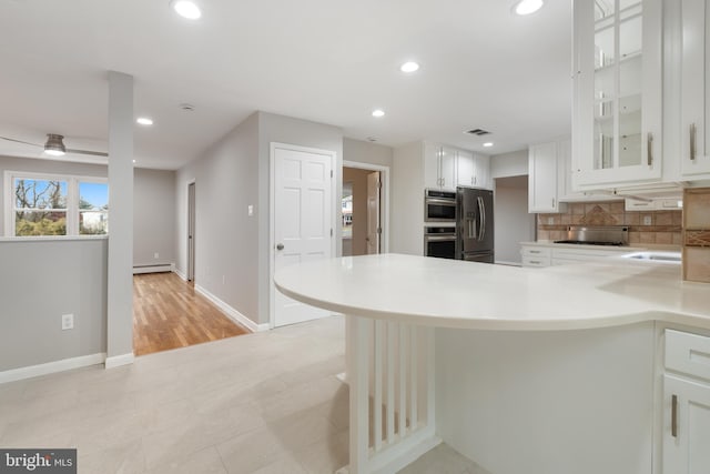 kitchen with ceiling fan, backsplash, white cabinetry, stainless steel appliances, and a baseboard radiator