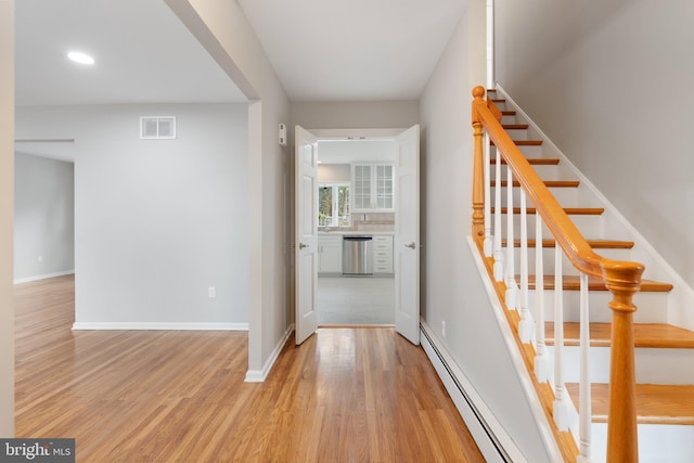 staircase with a baseboard heating unit and hardwood / wood-style floors