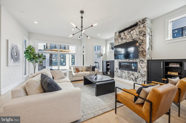 living room with wood-type flooring, a stone fireplace, and an inviting chandelier