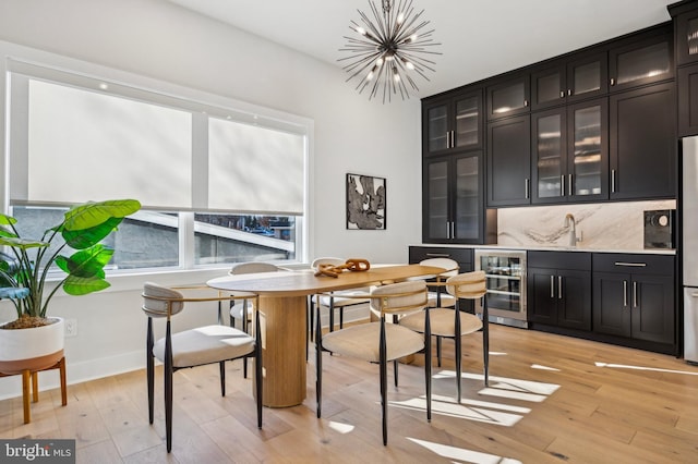 dining space with light hardwood / wood-style floors, bar area, beverage cooler, and an inviting chandelier