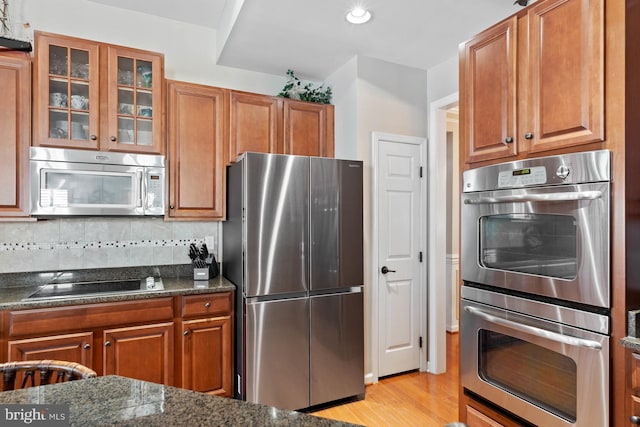 kitchen with decorative backsplash, light hardwood / wood-style flooring, stainless steel appliances, and dark stone countertops