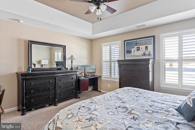 bedroom with ceiling fan, a tray ceiling, and light carpet