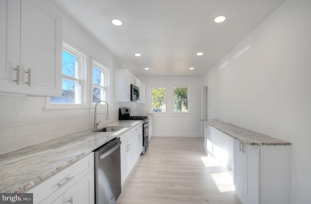 kitchen with white cabinetry, appliances with stainless steel finishes, backsplash, light stone countertops, and sink