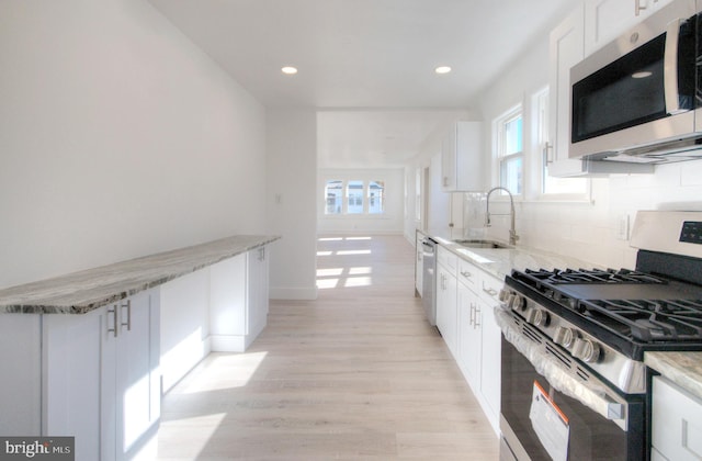 kitchen featuring white cabinetry, appliances with stainless steel finishes, light stone countertops, light hardwood / wood-style flooring, and sink