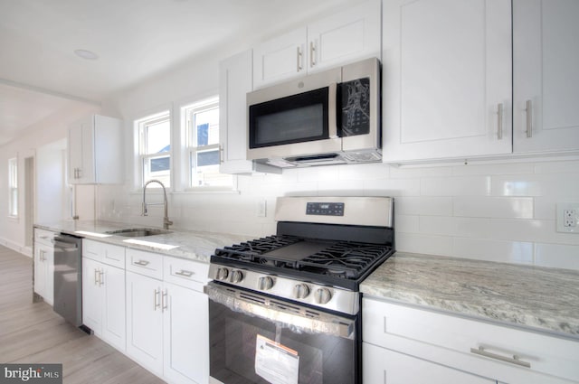 kitchen with stainless steel appliances, tasteful backsplash, light stone countertops, white cabinets, and sink