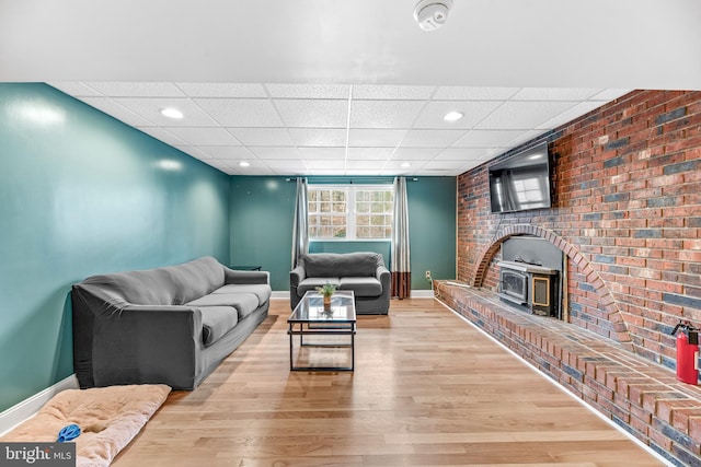 living room with a wood stove, light hardwood / wood-style flooring, and a drop ceiling