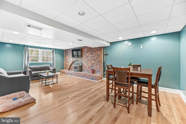 dining room featuring a paneled ceiling, wood-type flooring, and a wood stove