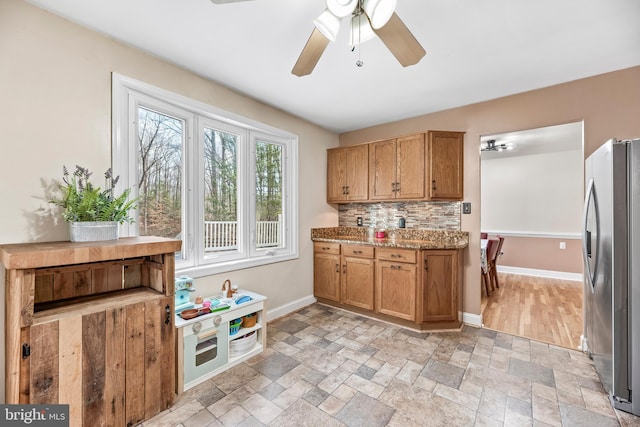 kitchen with tasteful backsplash, light stone counters, stainless steel refrigerator, and ceiling fan