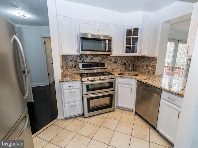 kitchen featuring appliances with stainless steel finishes, sink, white cabinetry, light stone counters, and decorative backsplash