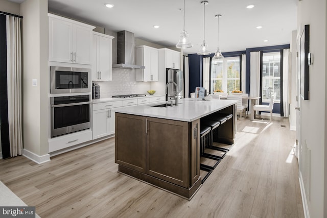 kitchen with sink, white cabinets, stainless steel appliances, a center island with sink, and wall chimney exhaust hood