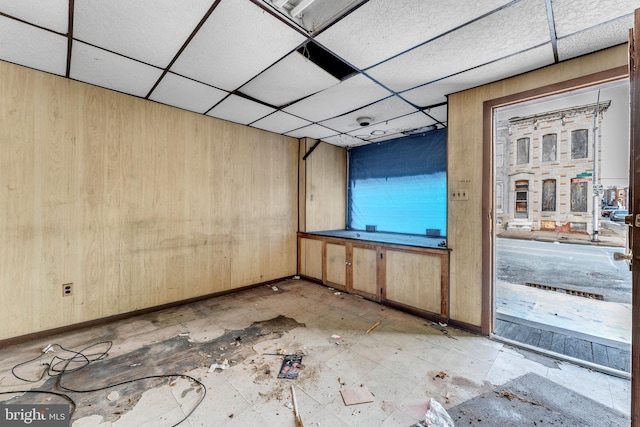 spare room featuring a drop ceiling and wooden walls