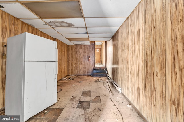 kitchen with baseboard heating, a drop ceiling, wood walls, and white fridge