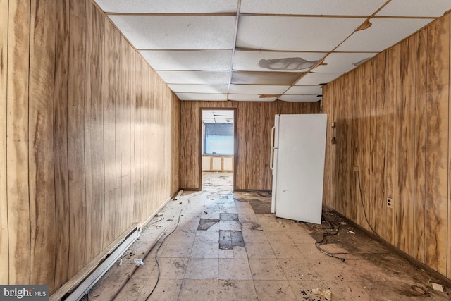 spare room featuring wood walls, baseboard heating, and a drop ceiling