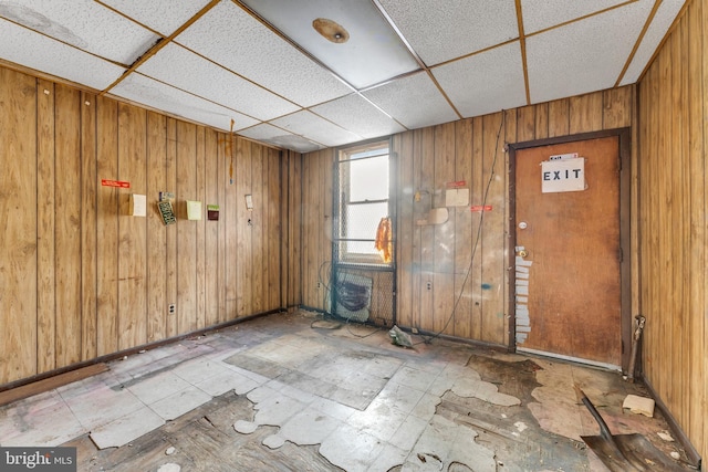 unfurnished room featuring wooden walls and a drop ceiling