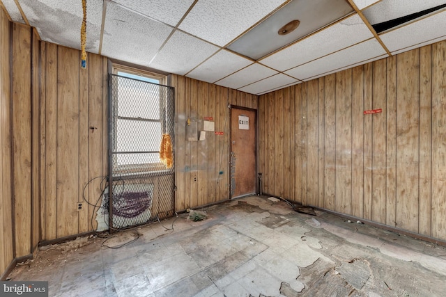 empty room featuring a paneled ceiling and wooden walls