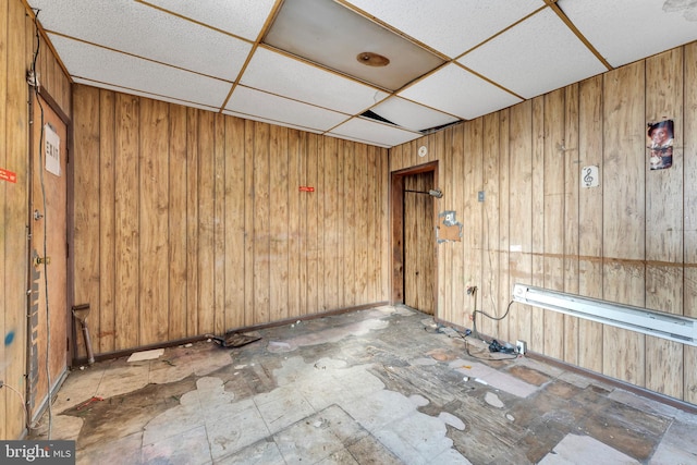 unfurnished room with a drop ceiling and wooden walls