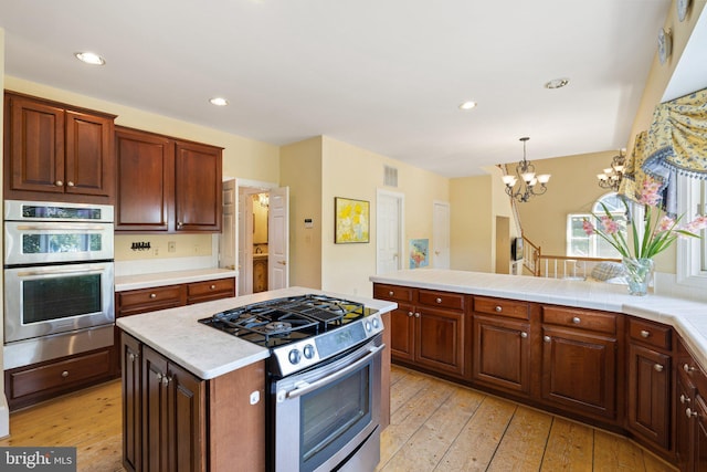 kitchen with an inviting chandelier, hanging light fixtures, stainless steel appliances, light hardwood / wood-style floors, and a kitchen island