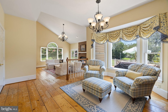 sitting room featuring lofted ceiling, hardwood / wood-style floors, a brick fireplace, and a notable chandelier