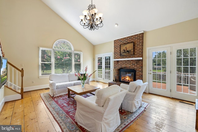 living room with an inviting chandelier, a brick fireplace, light hardwood / wood-style floors, and high vaulted ceiling