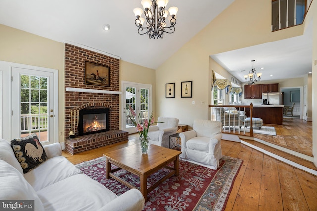 living room featuring an inviting chandelier, high vaulted ceiling, a brick fireplace, and light wood-type flooring