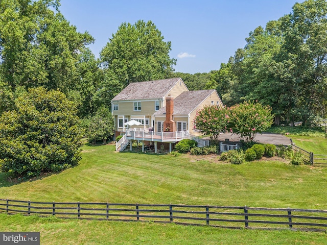 back of property featuring a rural view, a deck, and a lawn