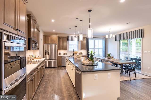 kitchen featuring backsplash, a center island, hanging light fixtures, appliances with stainless steel finishes, and dark wood-type flooring