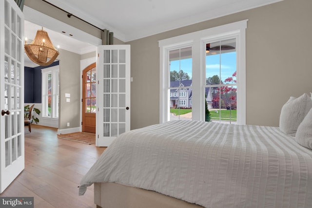 bedroom featuring light hardwood / wood-style flooring, french doors, ornamental molding, and multiple windows