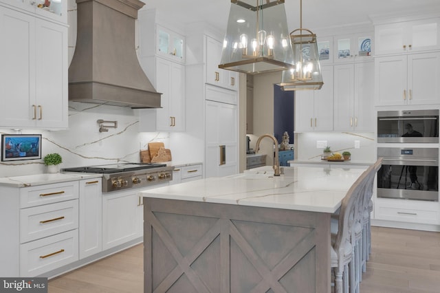 kitchen with sink, an island with sink, white cabinets, and custom range hood