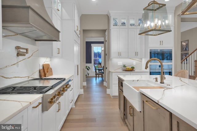 kitchen with hanging light fixtures, appliances with stainless steel finishes, premium range hood, white cabinetry, and light stone countertops