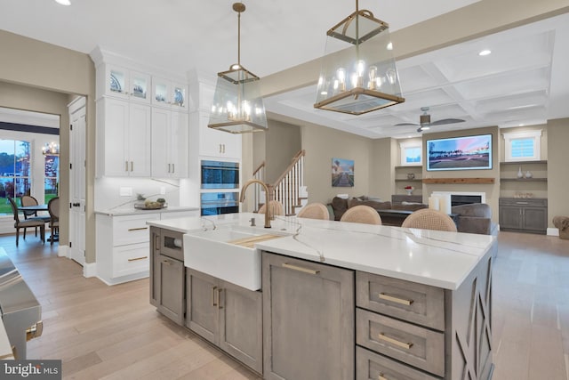 kitchen featuring beamed ceiling, coffered ceiling, hanging light fixtures, white cabinets, and an island with sink