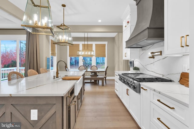 kitchen featuring decorative light fixtures, a large island with sink, white cabinets, and custom range hood