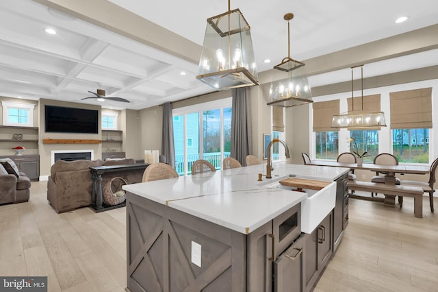 kitchen featuring an island with sink, hanging light fixtures, light hardwood / wood-style flooring, beam ceiling, and coffered ceiling