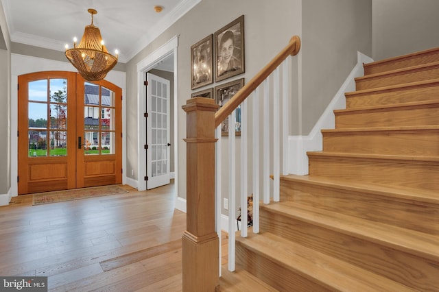 entryway with ornamental molding, a chandelier, light hardwood / wood-style flooring, and french doors