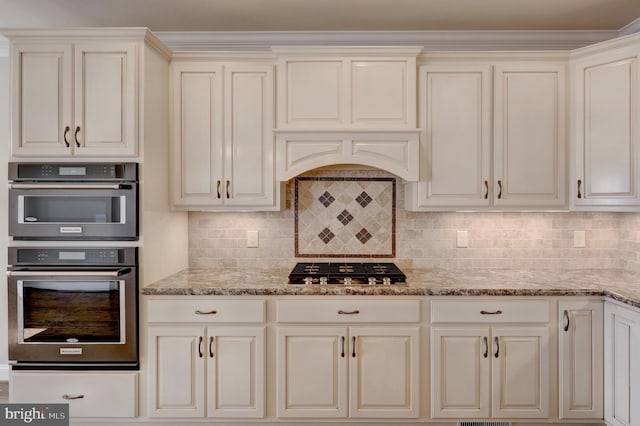 kitchen featuring multiple ovens, stainless steel gas cooktop, decorative backsplash, and light stone counters