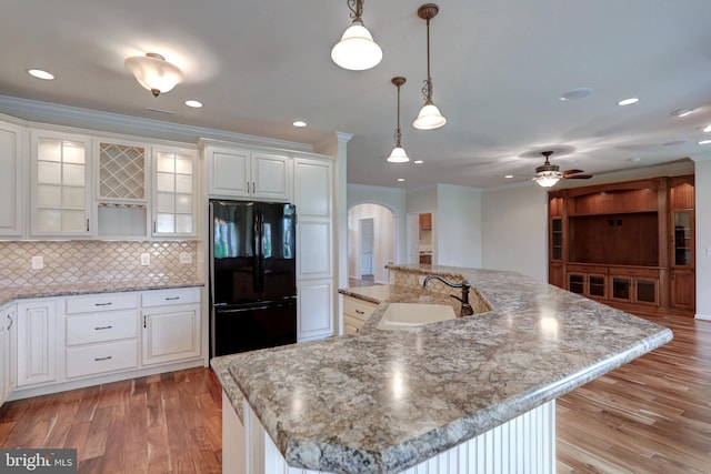 kitchen with black refrigerator, a large island, hanging light fixtures, white cabinets, and sink