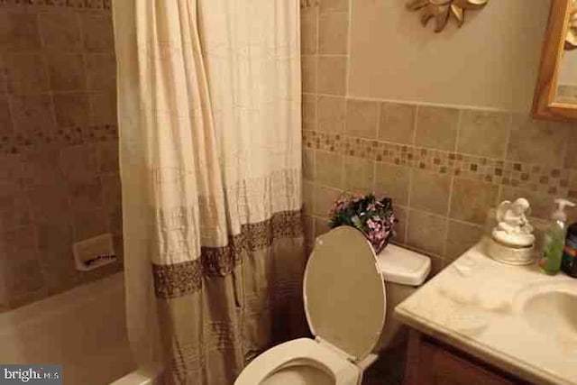 full bathroom featuring toilet, tile walls, vanity, and shower / tub combo with curtain