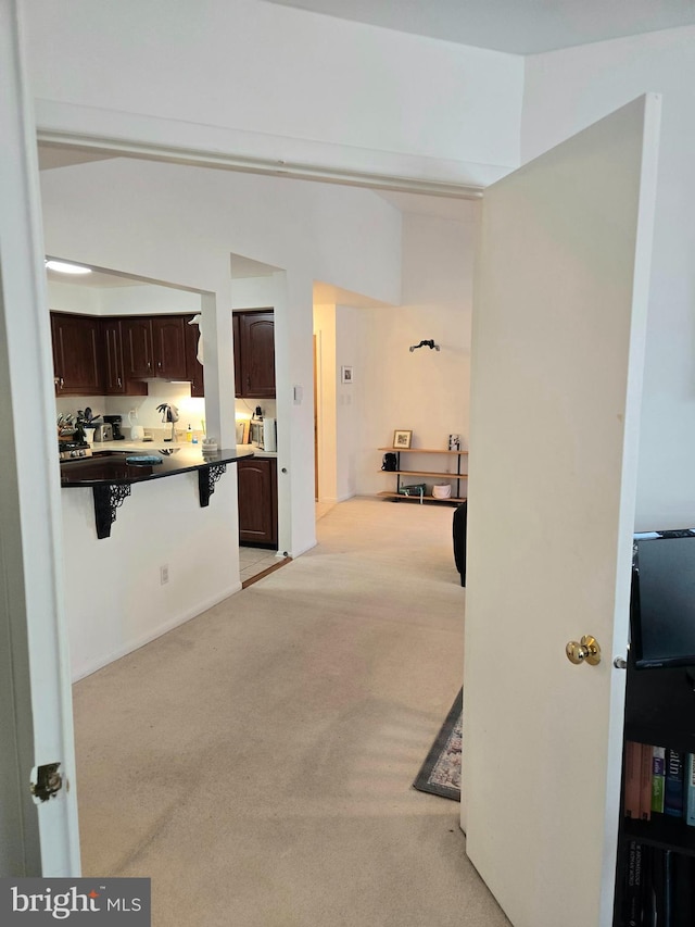 kitchen with light colored carpet, dark brown cabinetry, and a kitchen bar