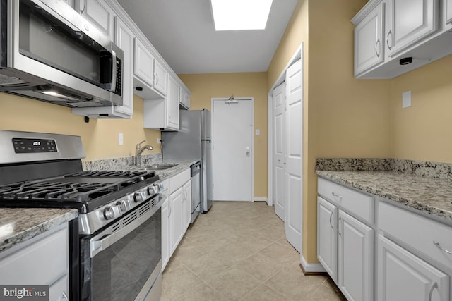 kitchen featuring light tile patterned flooring, sink, appliances with stainless steel finishes, light stone countertops, and white cabinets