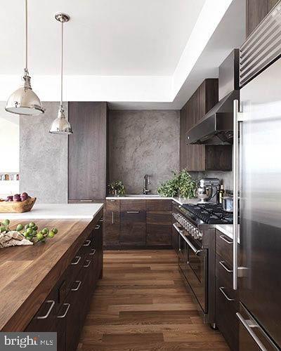 kitchen featuring wall chimney range hood, dark hardwood / wood-style flooring, dark brown cabinets, and high end appliances