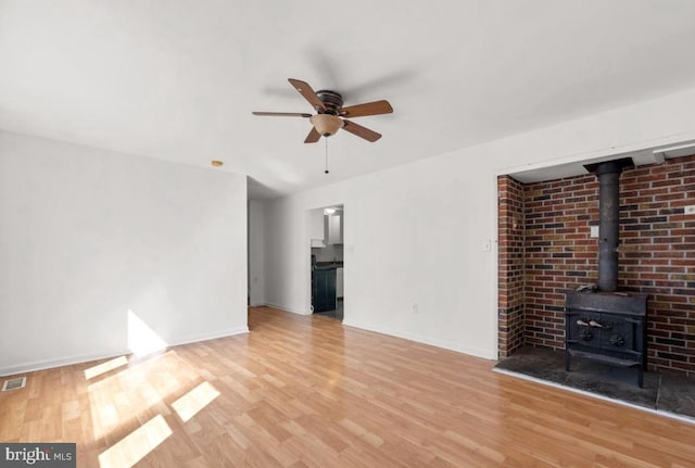 unfurnished living room featuring ceiling fan, a wood stove, and light hardwood / wood-style flooring