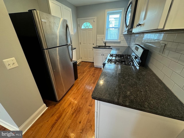 kitchen featuring wood-type flooring, sink, white cabinets, decorative backsplash, and stainless steel appliances