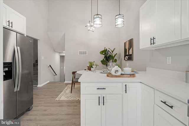 kitchen with stainless steel fridge with ice dispenser, hanging light fixtures, light wood-type flooring, kitchen peninsula, and white cabinets