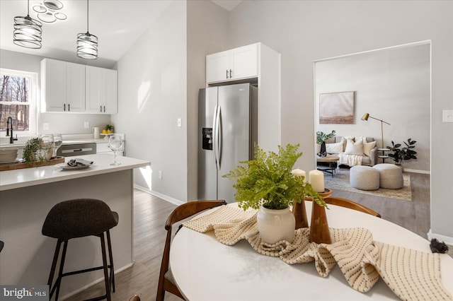 kitchen with stainless steel fridge, a breakfast bar area, wood-type flooring, white cabinets, and decorative light fixtures