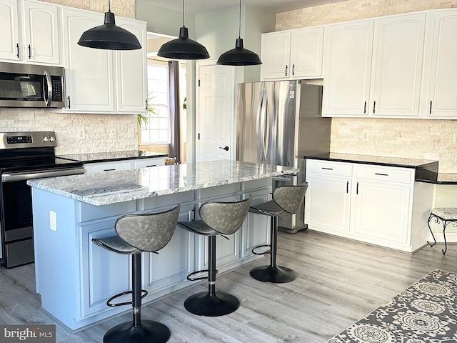 kitchen with dark stone countertops, stainless steel appliances, hanging light fixtures, and white cabinets