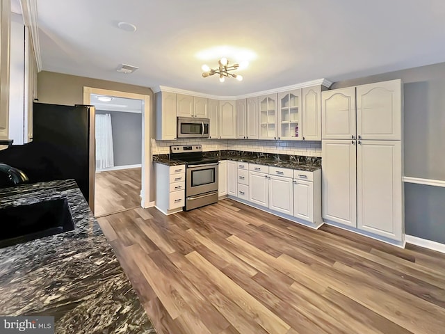 kitchen featuring decorative backsplash, light wood-style flooring, glass insert cabinets, appliances with stainless steel finishes, and a sink