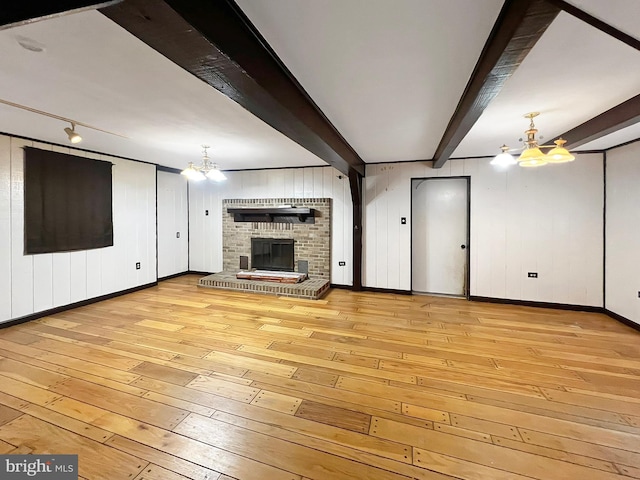 unfurnished living room with a notable chandelier, a fireplace, baseboards, light wood-type flooring, and beamed ceiling