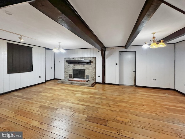 unfurnished living room with light wood-style floors, a fireplace, beam ceiling, and an inviting chandelier