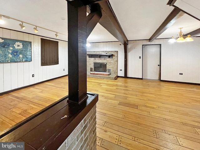 unfurnished living room with light wood-type flooring, beam ceiling, a fireplace, and baseboards