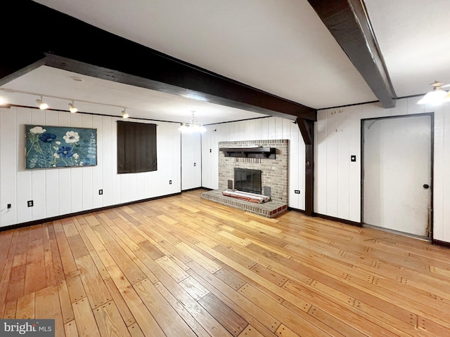 unfurnished living room featuring baseboards, light wood-style floors, a brick fireplace, beam ceiling, and rail lighting