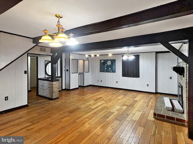 interior space featuring visible vents, light wood-type flooring, a fireplace, a chandelier, and beam ceiling